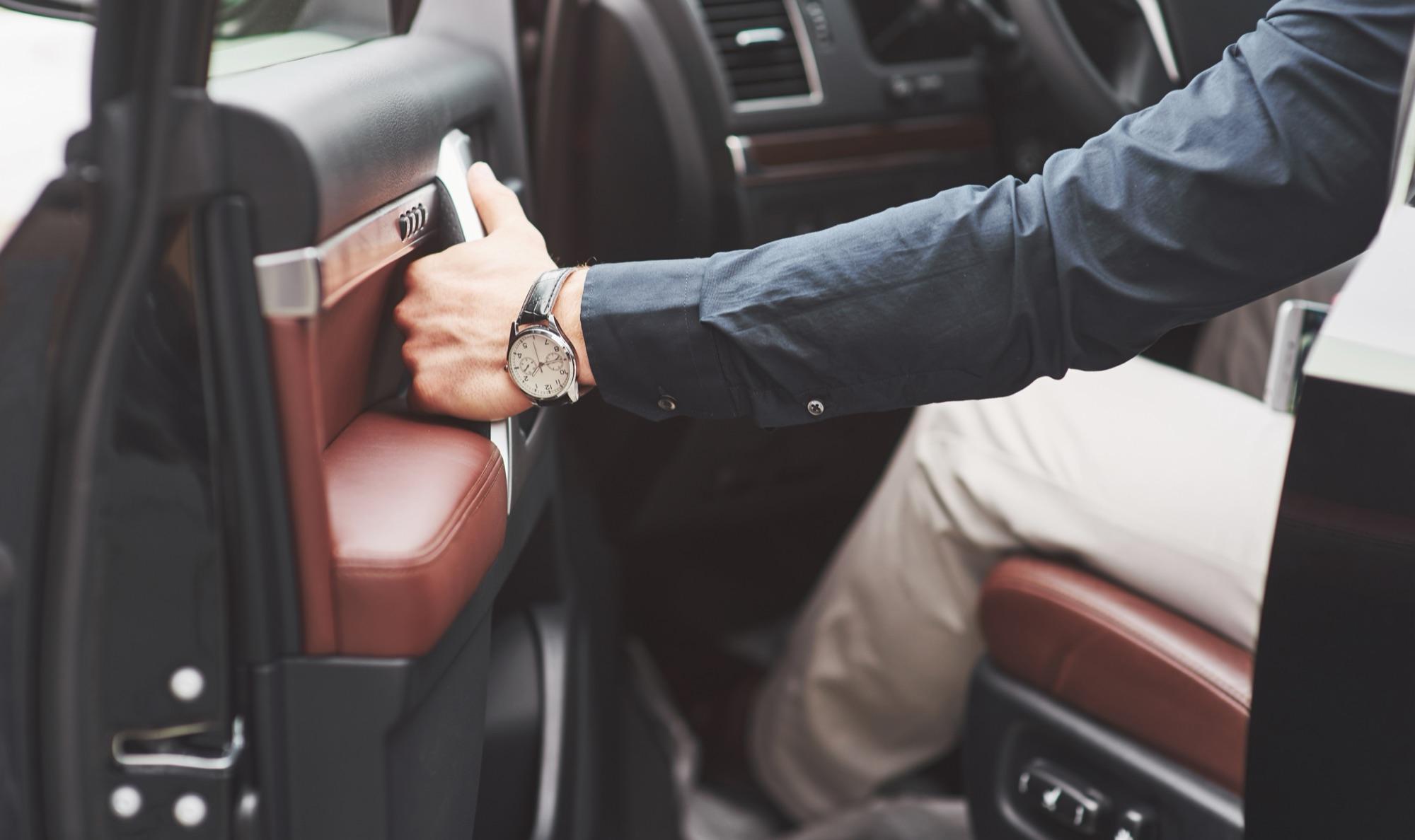 Chauffeur in maatpak opent het portier van een luxewagen